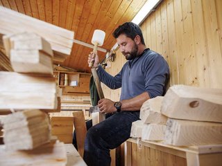 Mit Spalteisen und Holzschlägel spaltet Schindelmacher Tristan Ropraz das Holz. Zu seiner Linken warten die so genannten Weggen auf ihre Verarbeitung.
