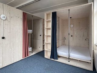 Hölzerne Kammern mit Etagenbetten oder Doppelbetten generieren Räume im Raum. Vorhänge dienen als Sichtschutz.
